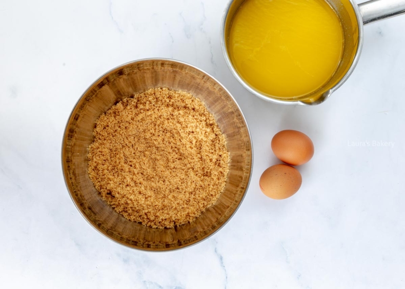 Melted butter in a jug and sugar in a mixing bowl with loose eggs on the countertop.