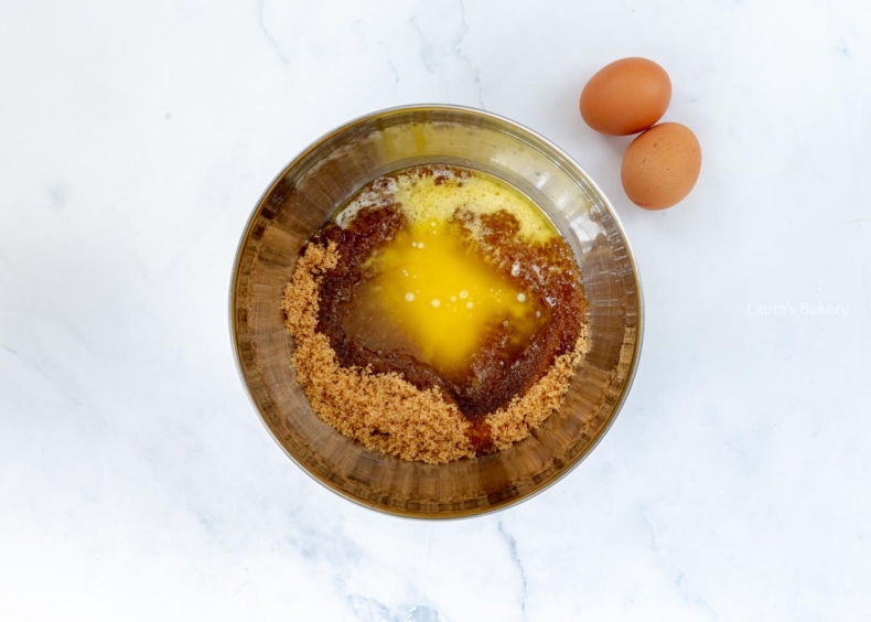 Light brown sugar, melted butter in a mixing bowl with loose eggs on the countertop.